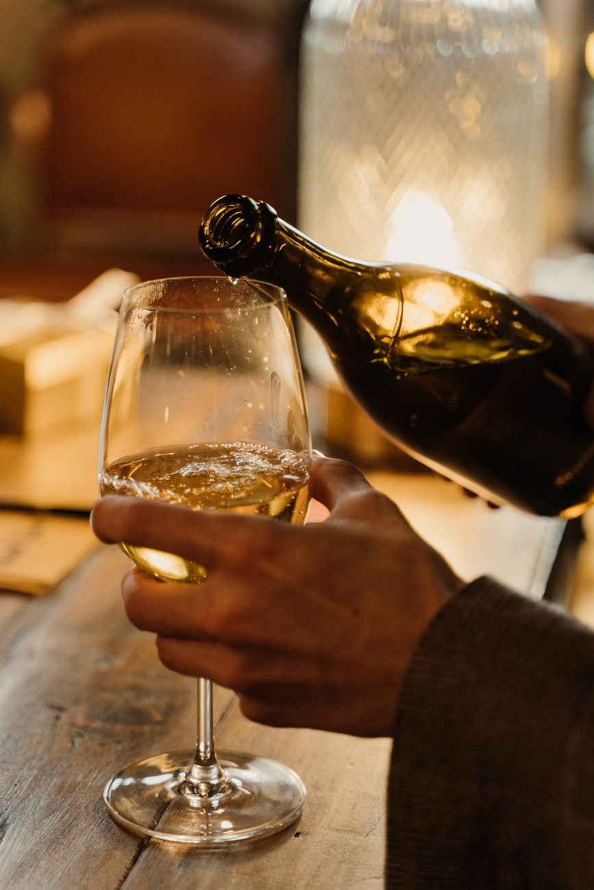 Elegant close-up of white wine being poured into a glass indoors with warm lighting.